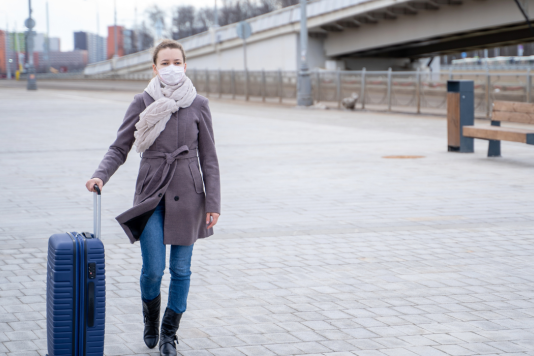 A woman wearing a mask holding luggage 